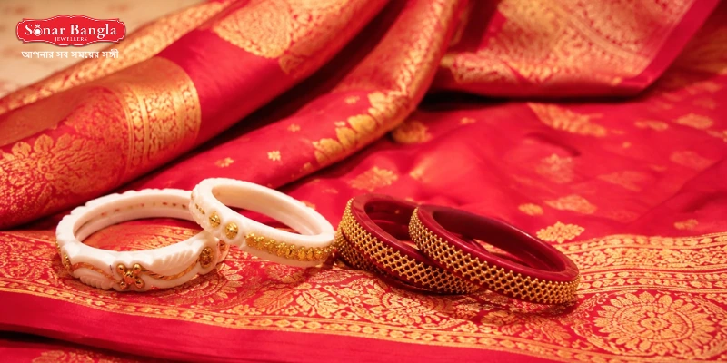 Traditional white sankha and red pola bangles with beautiful gold leaf embossments laid over a luxurious red banarasi bridal saree.